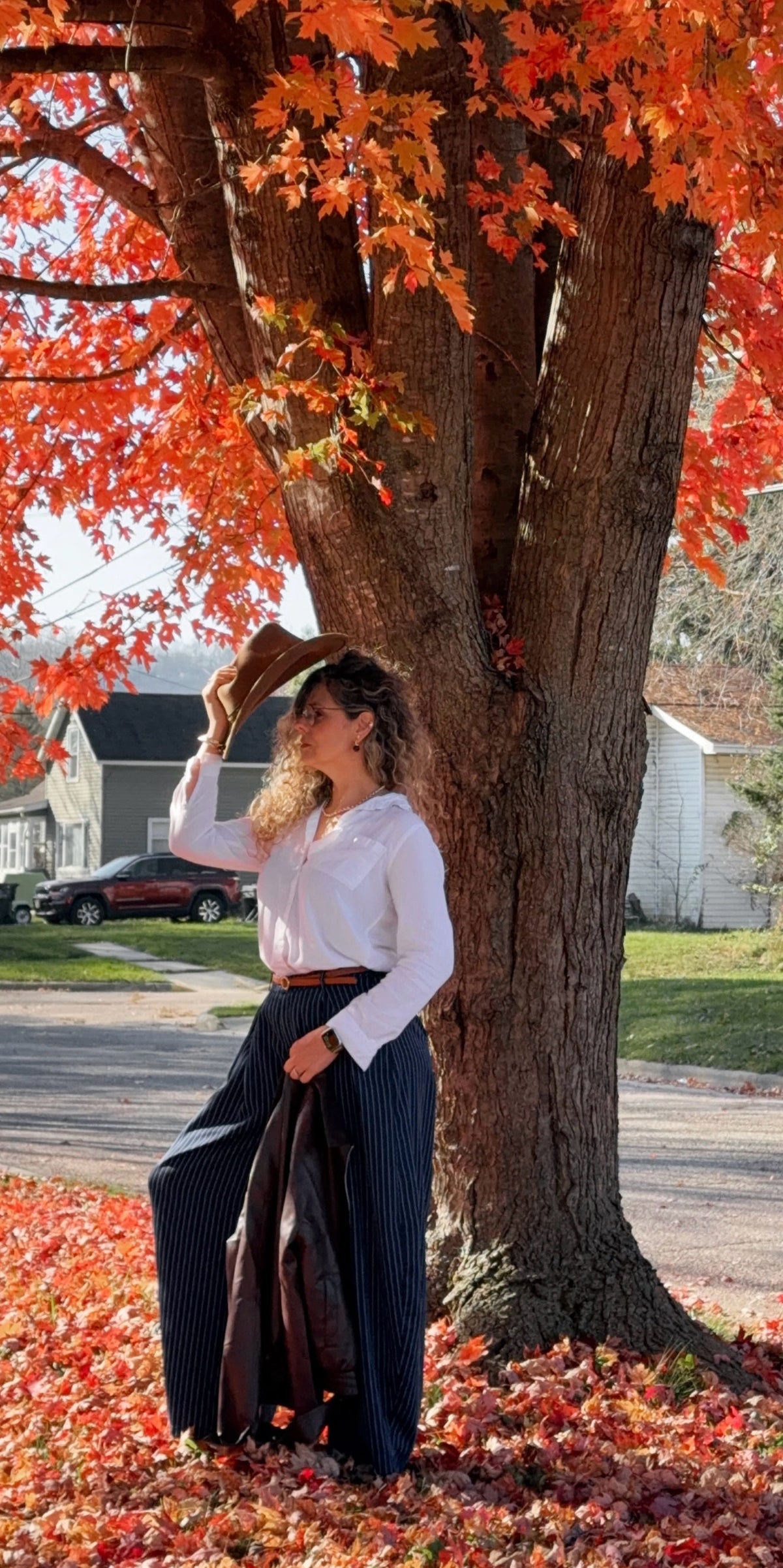 Lu de pie junto al árbol de hojas rojas, con el sombrero en la mano
